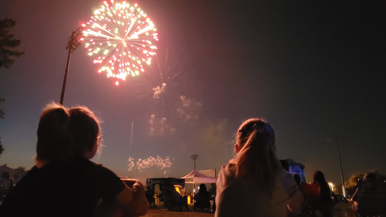 Two people silhouetted against a night sky watching fireworks over Gahagan Park.