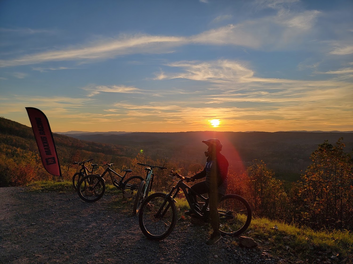 Mountain bikes parked along a ridge at sunset, a rider silhouetted against an orange sky.