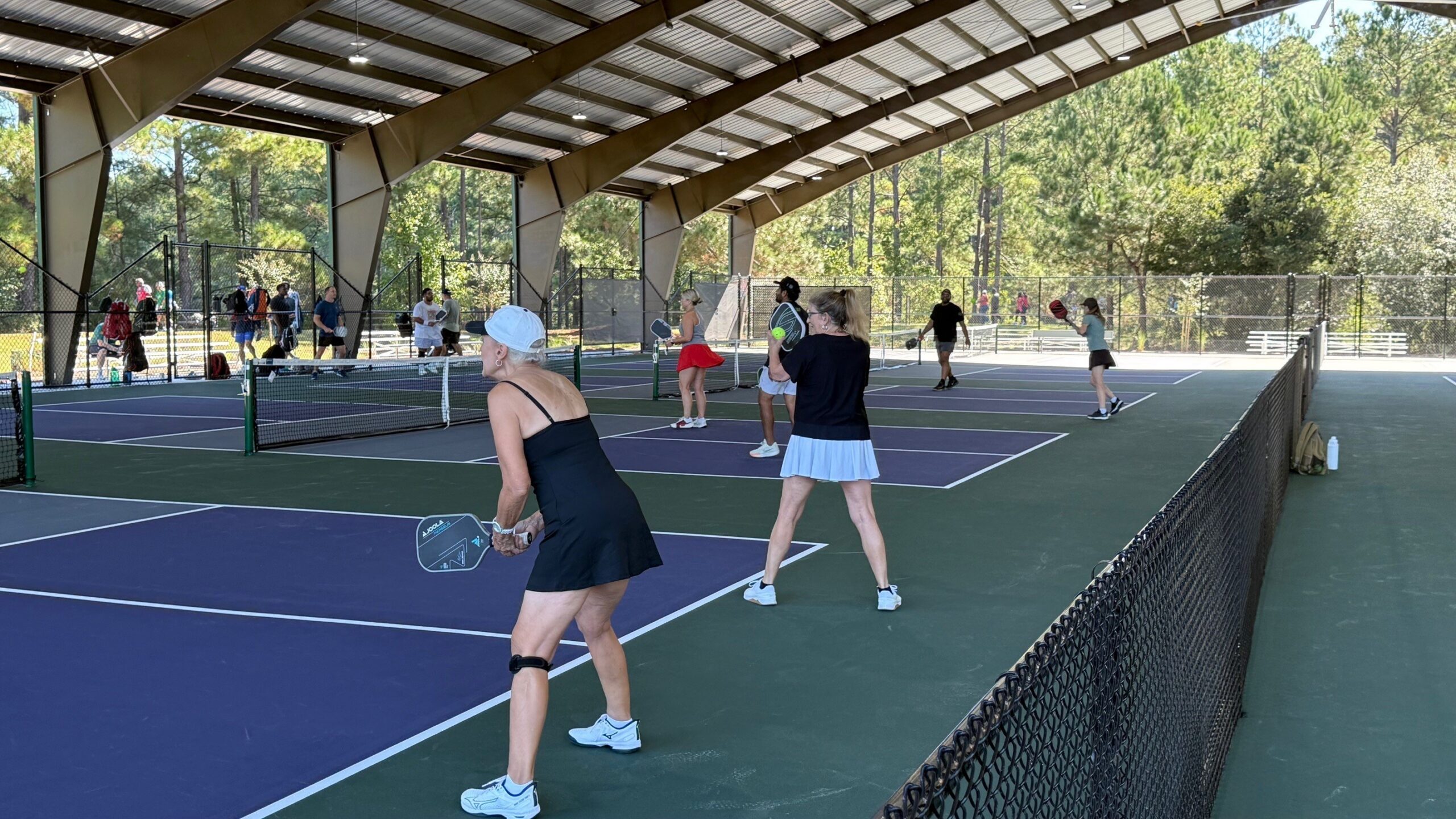 a doubles game under the covered courts, fans and roof overhead