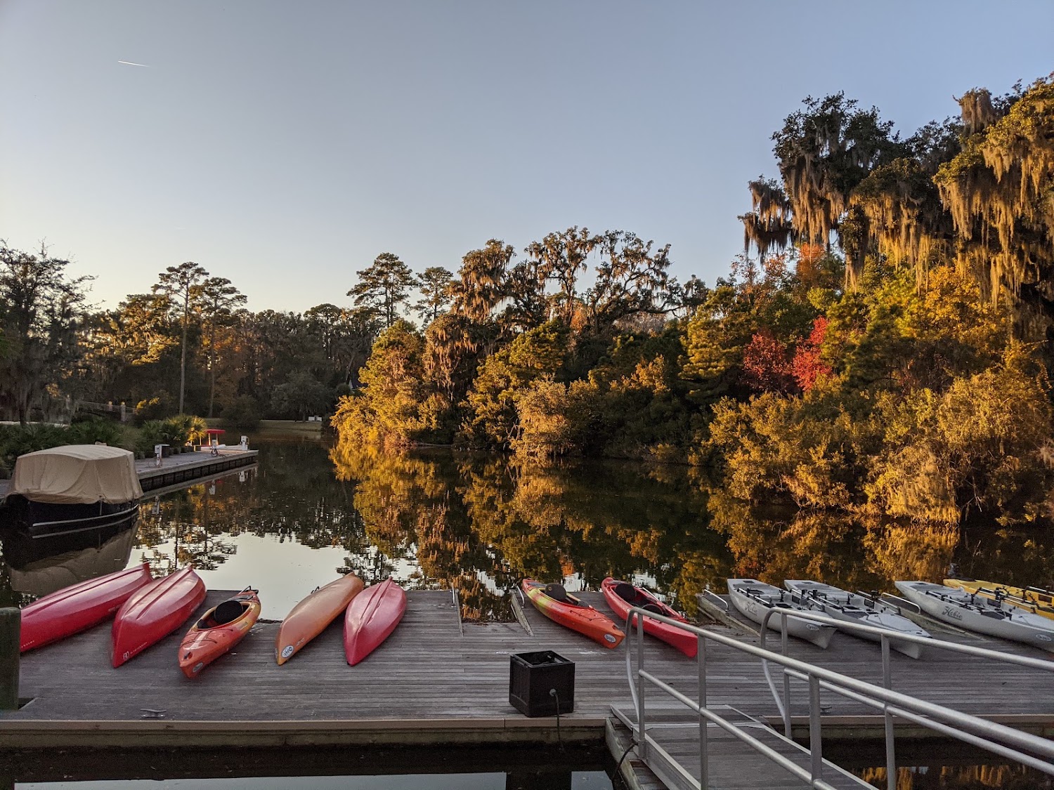Kayaks racked on a wooden dock at golden hour, the river still and moss-hung trees on the far bank.