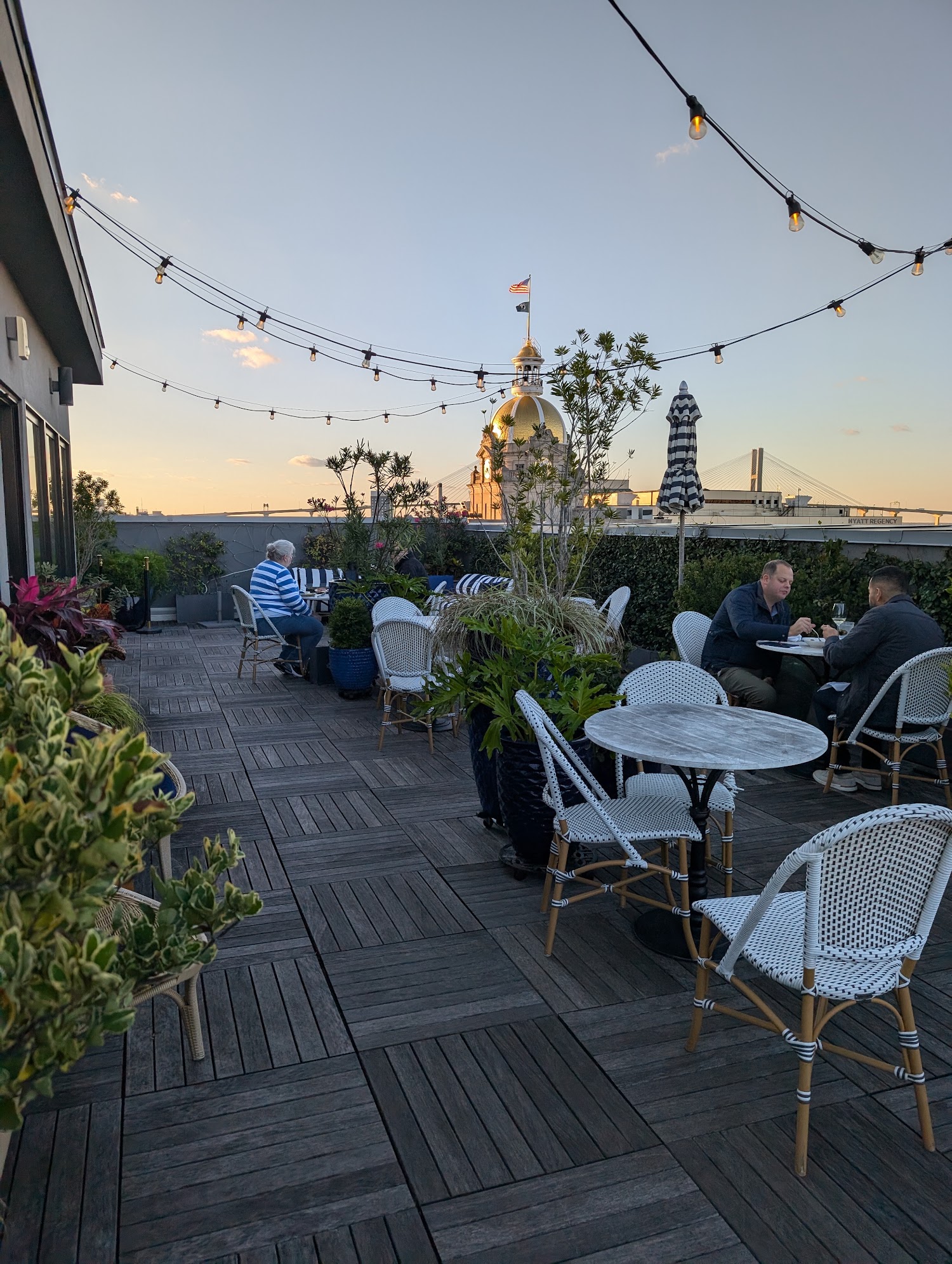 The Pendant terrace at dusk, tables under strung lights with the lit dome of Savannah City Hall beyond.