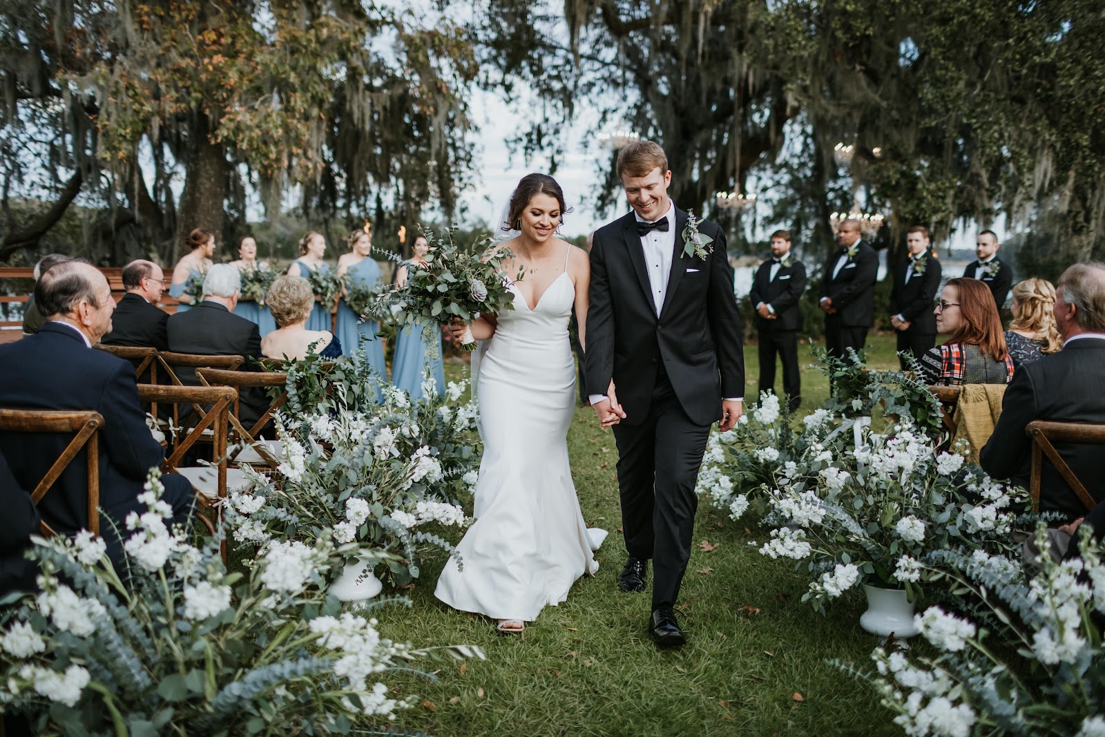 A couple walking an aisle lined with white flowers