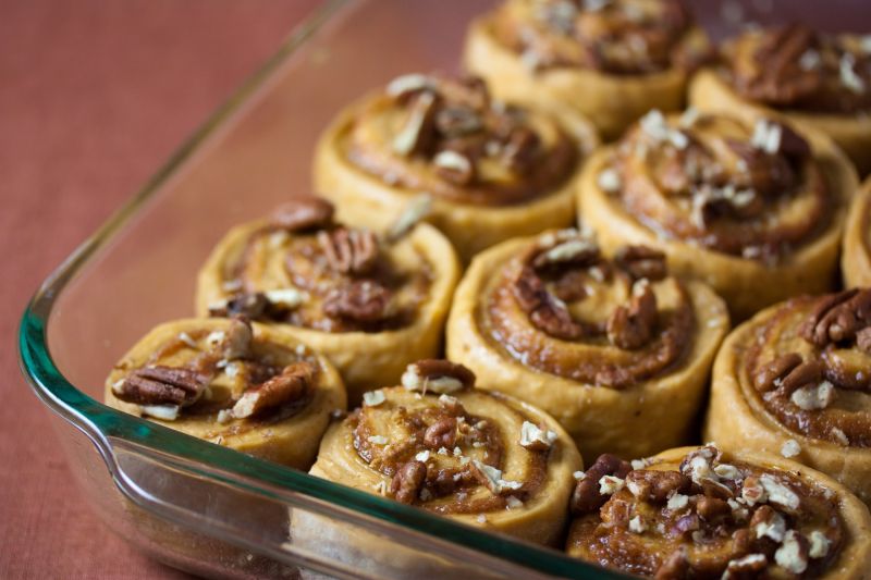 A glass baking dish of pumpkin cinnamon rolls topped with chopped pecans and a caramel glaze