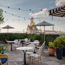 The rooftop terrace of the Pendant bar in Savannah at golden hour, string lights overhead and the gold dome of City Hall behind it.